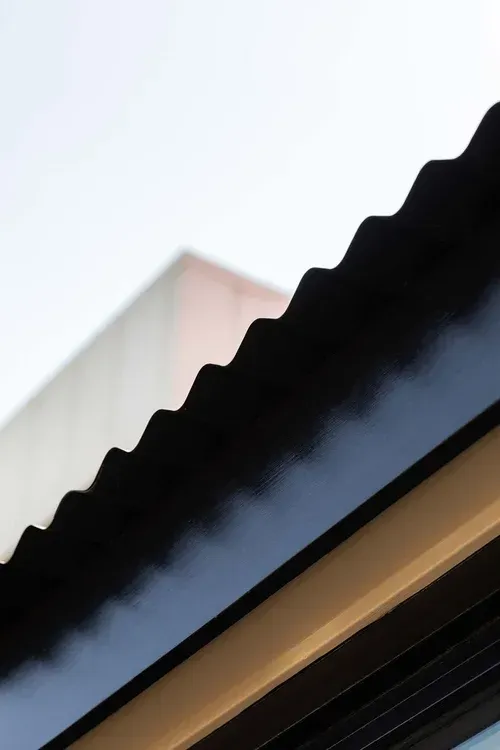 Close-up of a black scalloped awning against a pale sky and building facade
