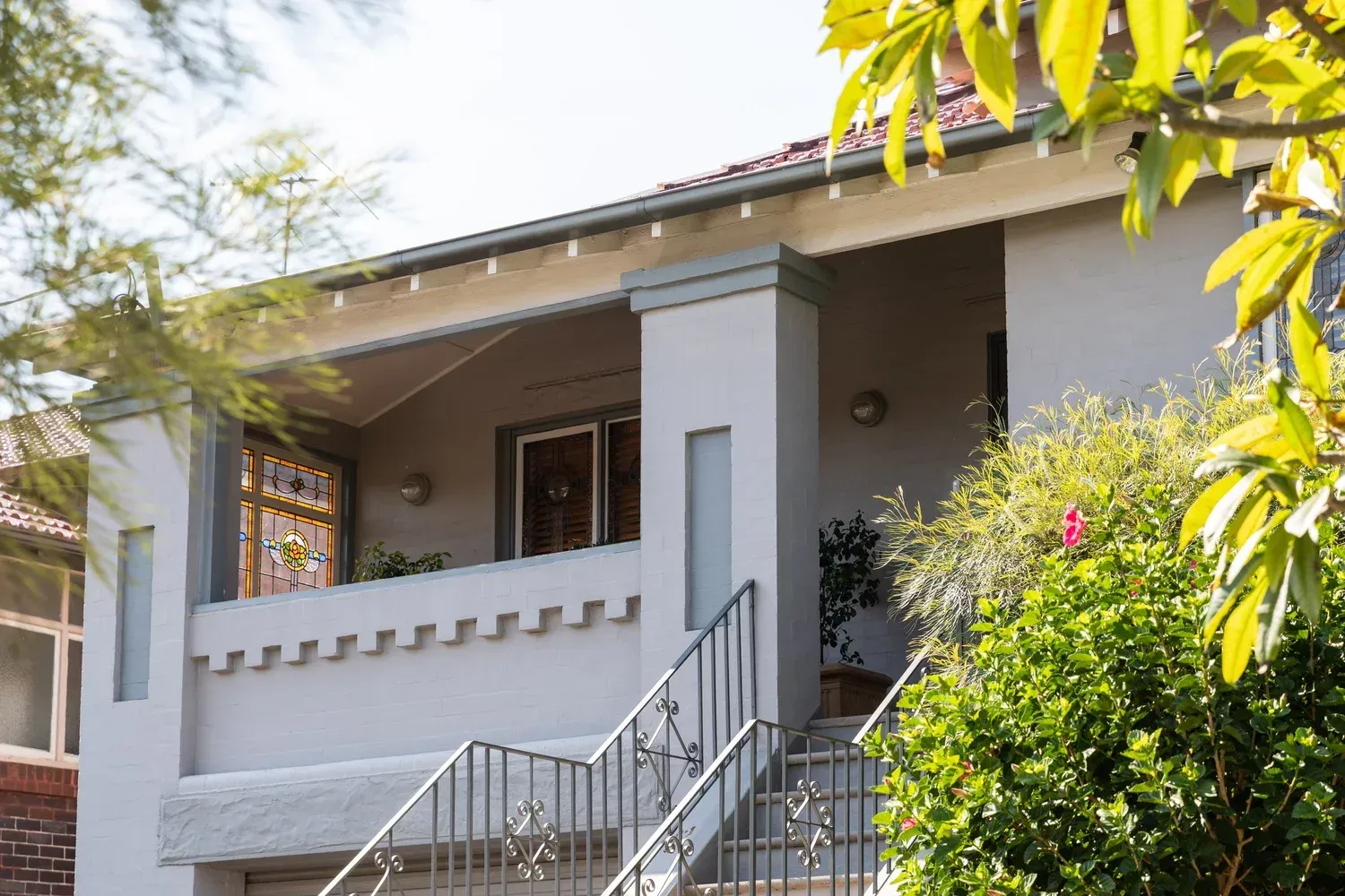 Front porch of a gray house with white trim, stairs, and leafy trees around it