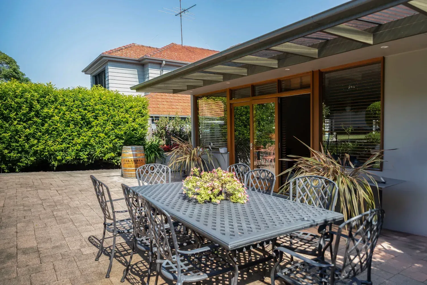 Patio with metal table and chairs under a covered patio beside a house and hedge