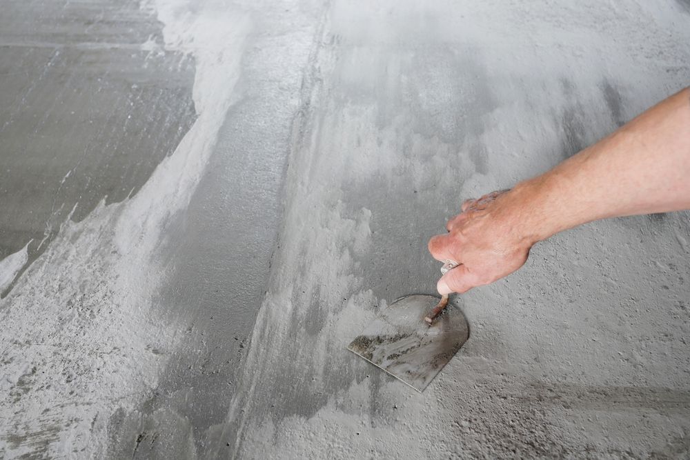 A freshly laid, smooth gray concrete floor in an unfinished room with light-colored walls and visible wall outlets 