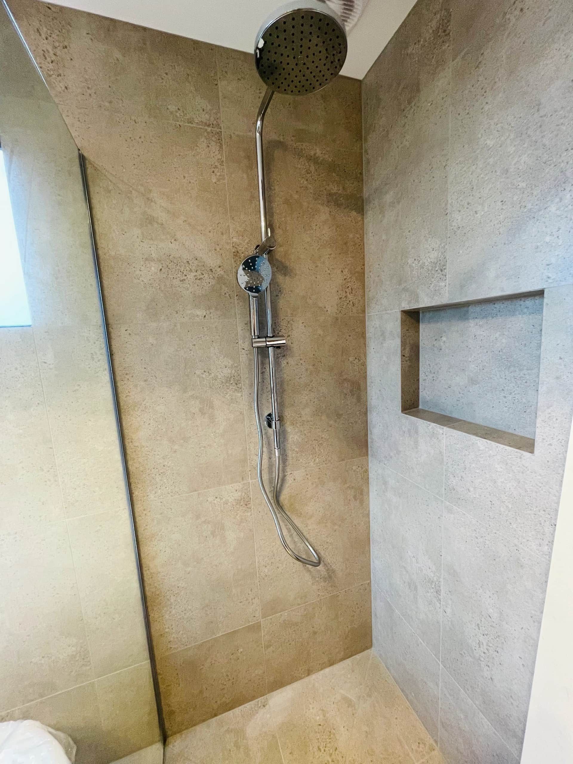 A walk-in shower with beige tiled walls, a silver rain showerhead on a slide bar, and a rectangular wall niche. — Hobart Tiling Solutions In Clarendon Vale, TAS