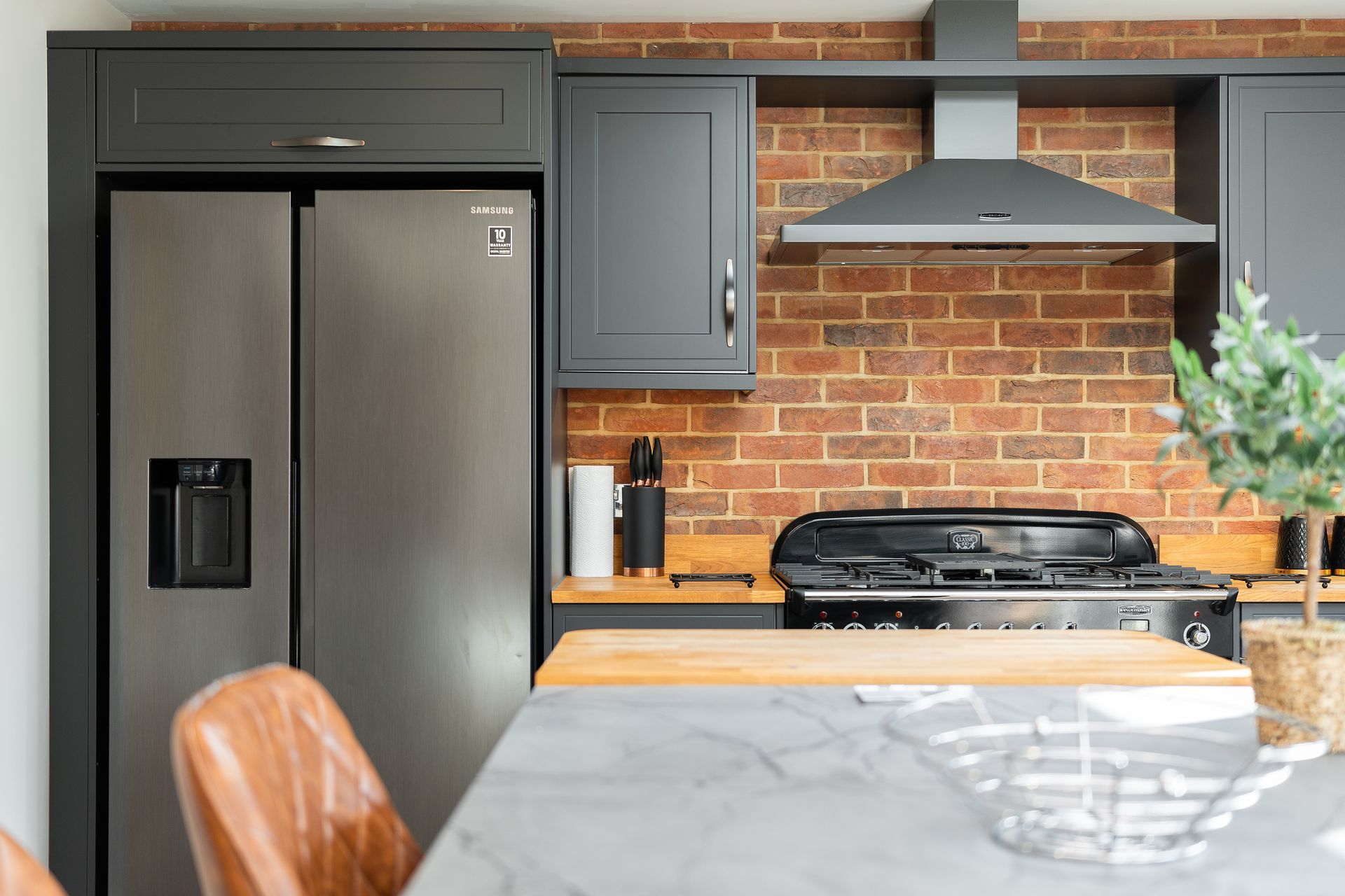 A kitchen with a refrigerator , stove , and a brick wall.