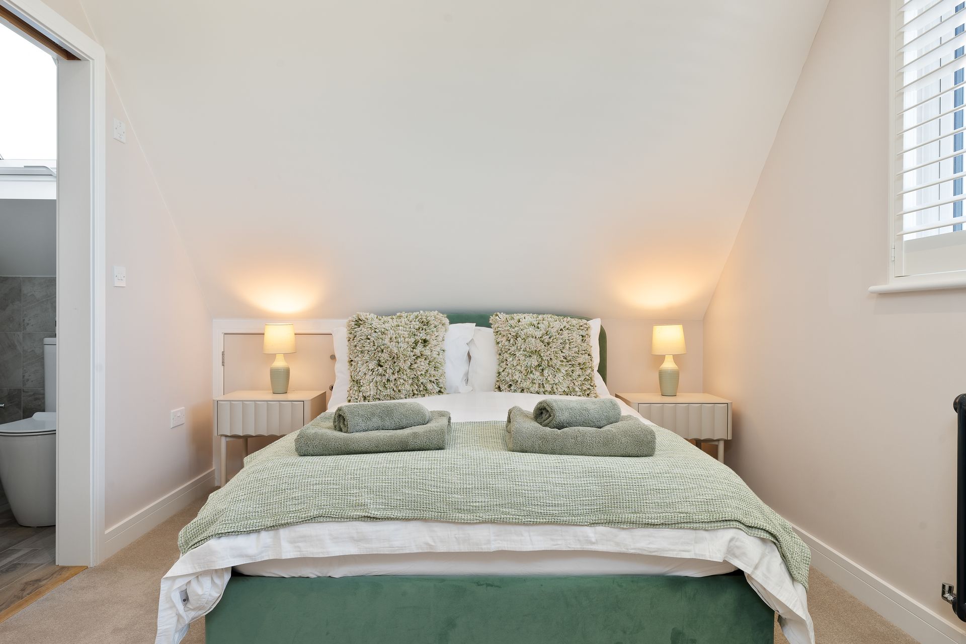 A bedroom with a bed , two nightstands , two lamps and a window.