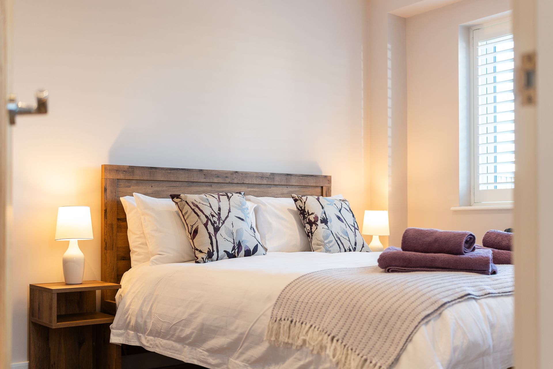 A bedroom with a bed , two lamps , and a window.