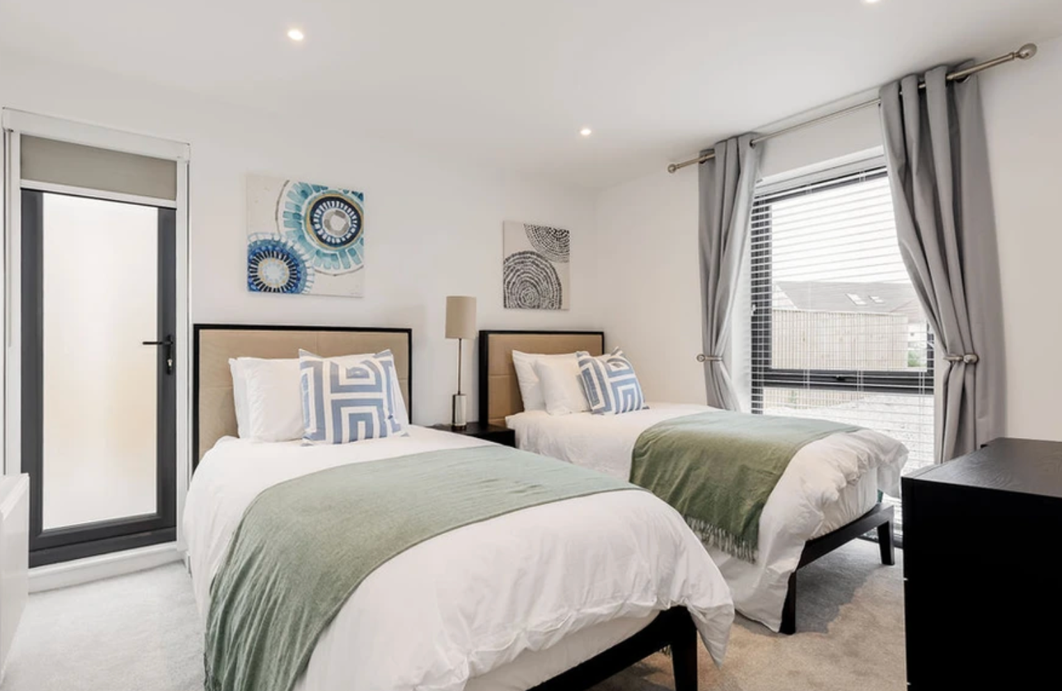 A bedroom with two beds , a dresser and a window.