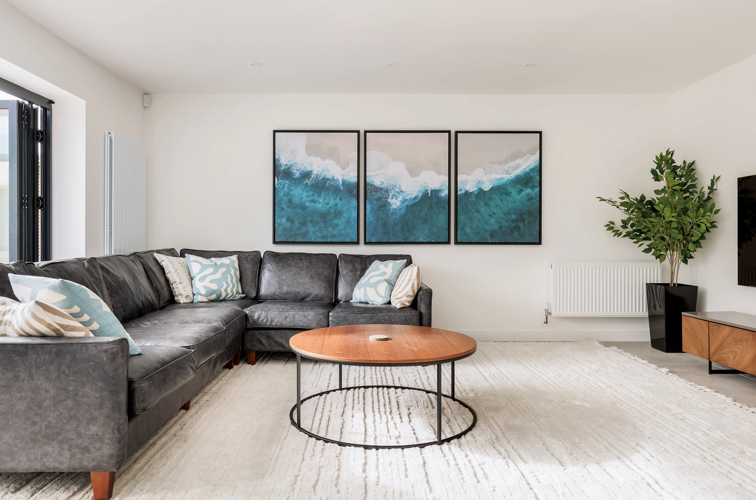 A living room with a large sectional couch , coffee table , and paintings on the wall.