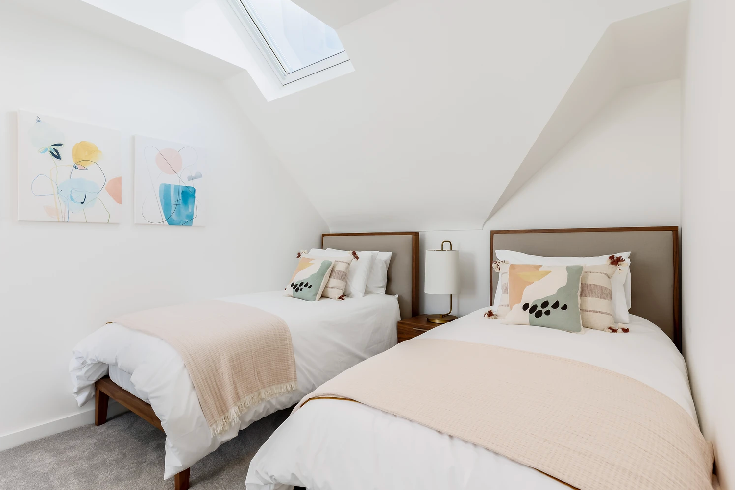 A bedroom with two beds and two paintings on the wall.