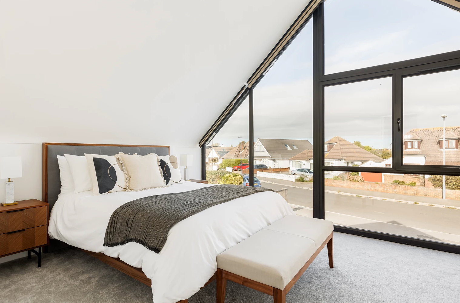 A bedroom with a king size bed and a bench in front of a large window.