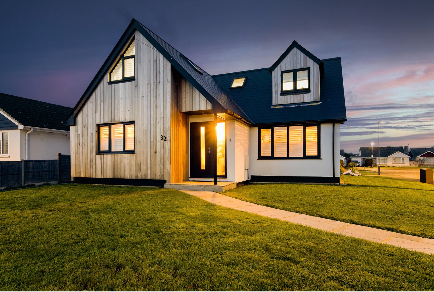 A house with a blue roof and a lot of windows is lit up at night.