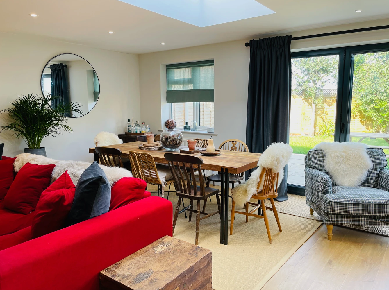 A living room with a red couch , chairs , a table and a mirror.