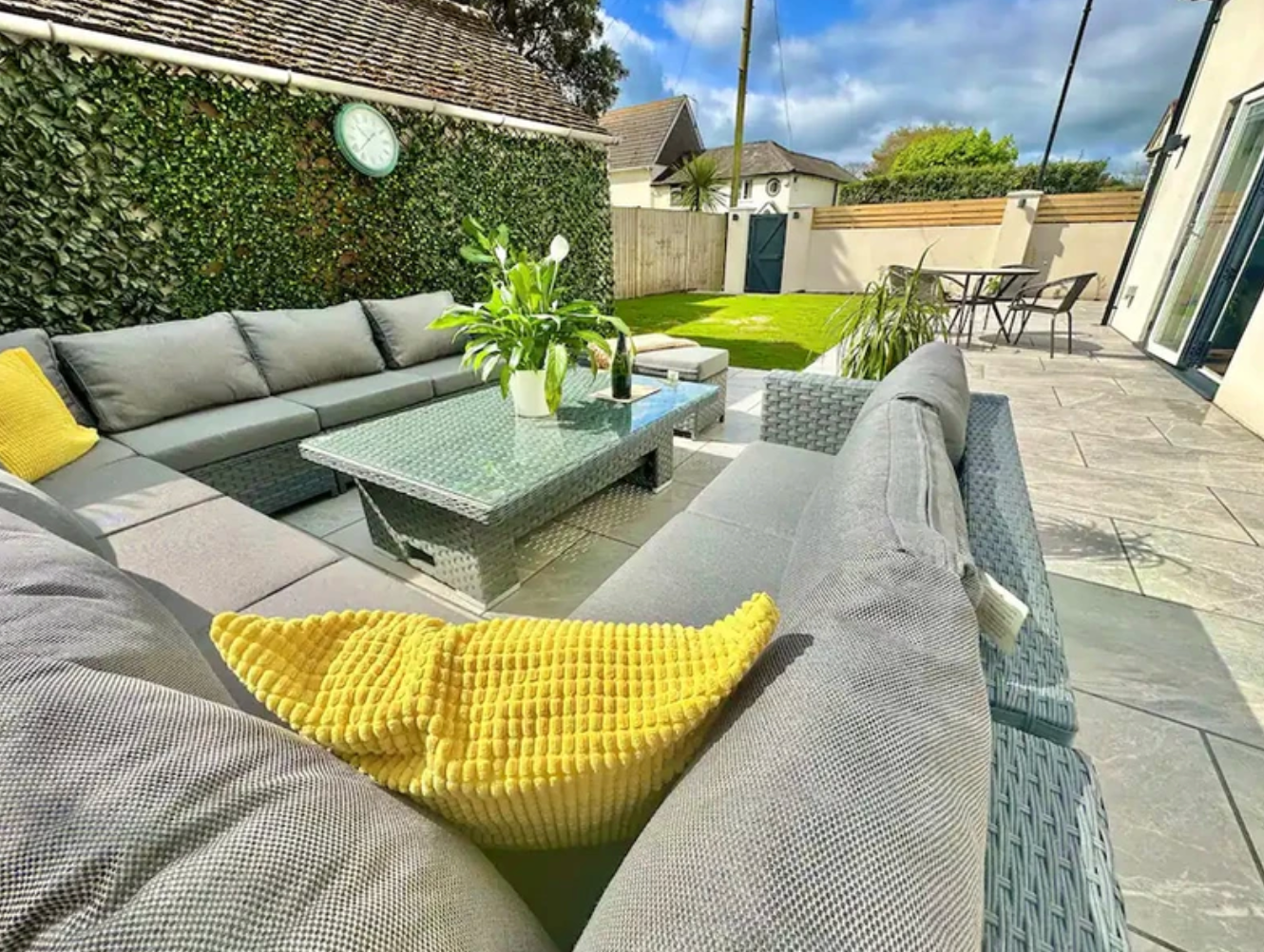 A patio with a couch , table , chairs and a yellow pillow.