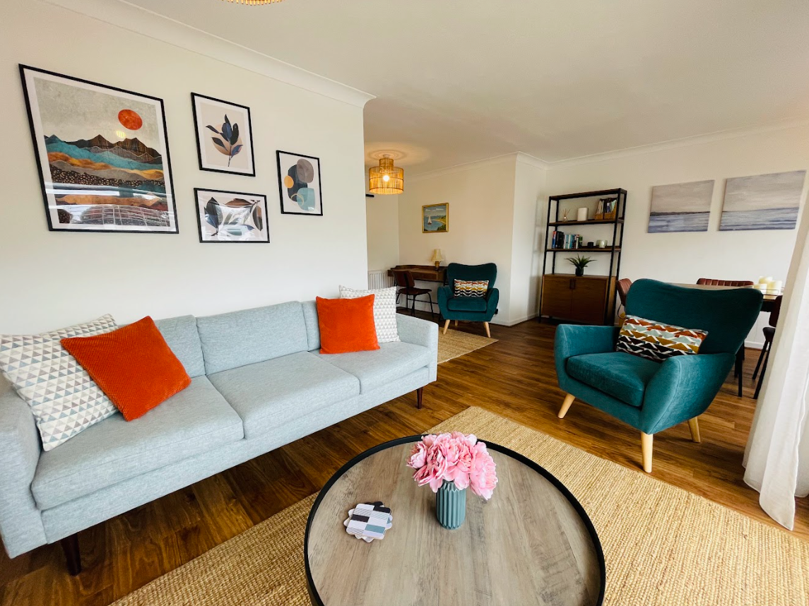 A living room with a couch , chair , coffee table and paintings on the wall.