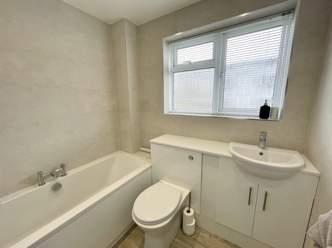 A bathroom with a toilet , sink , bathtub and window.