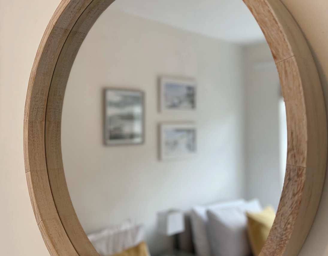 A round mirror with a wooden frame is hanging on a wall