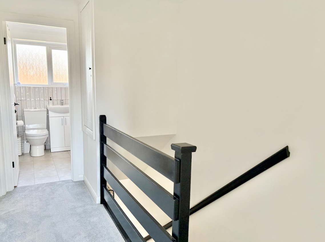 A hallway with a black railing leading to a bathroom