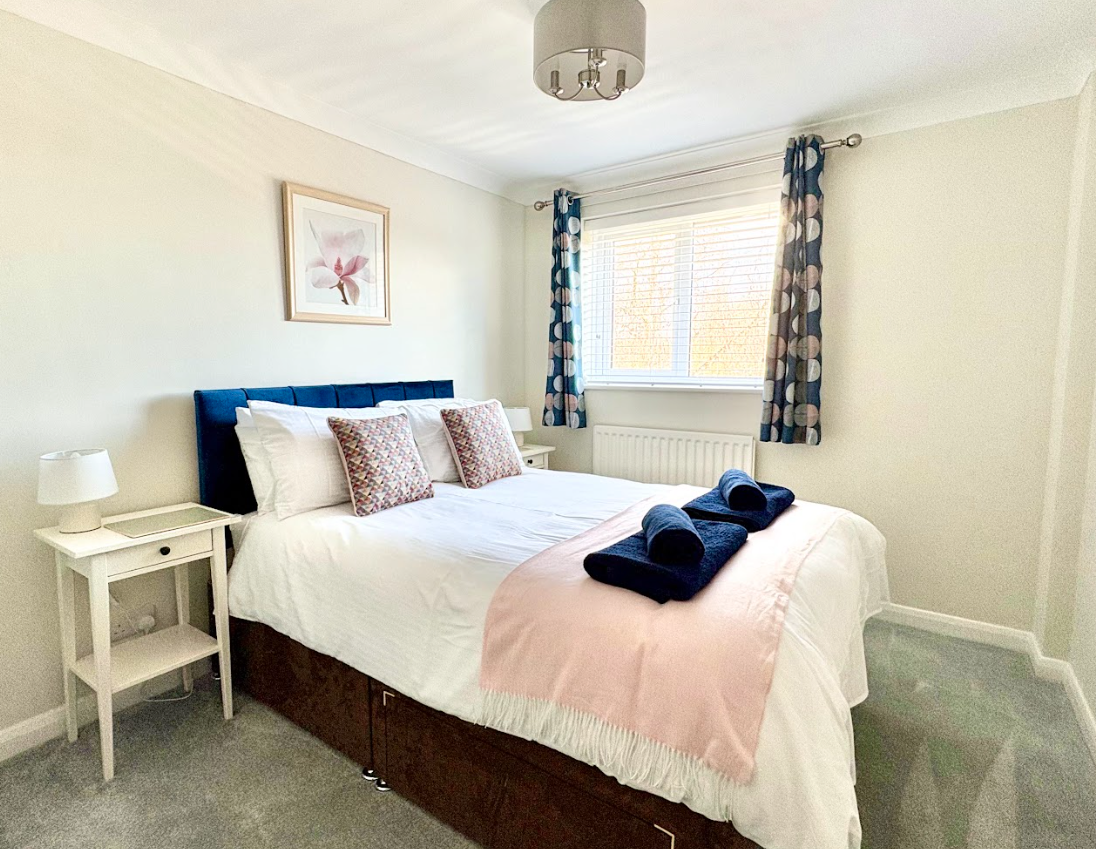 A bedroom with a bed , nightstand , lamp and window.