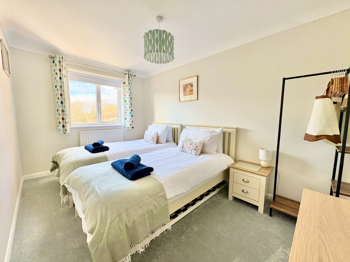 A bedroom with two twin beds , a nightstand , a lamp and a window.