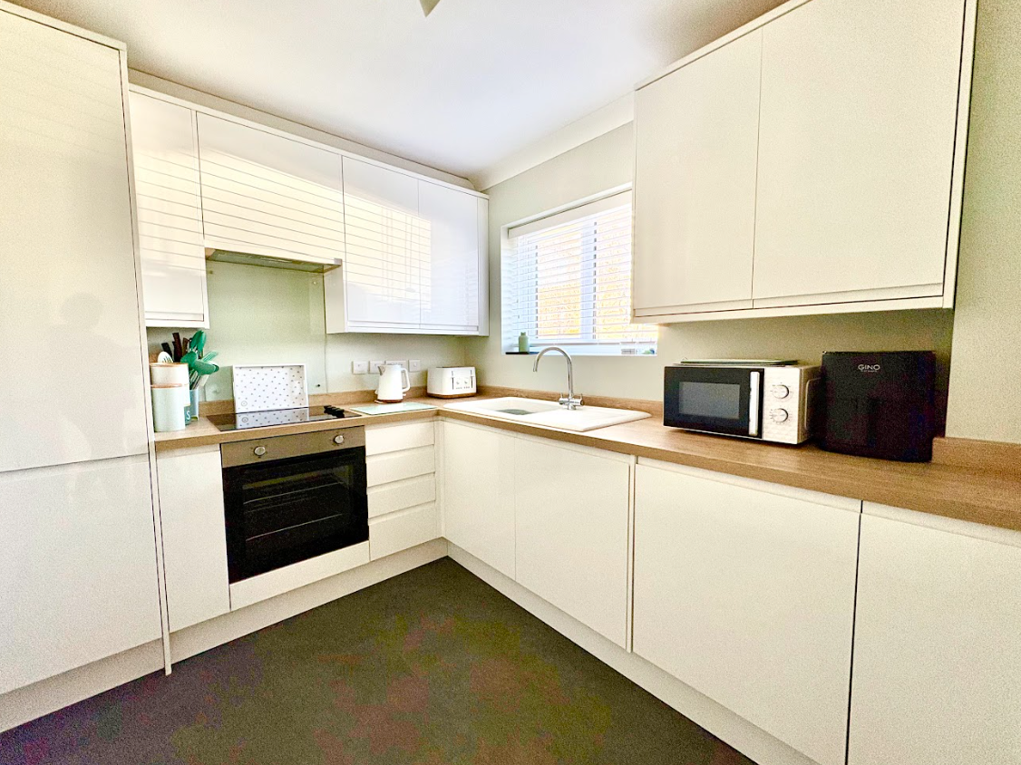 A kitchen with white cabinets , a stove , a microwave , and a sink.