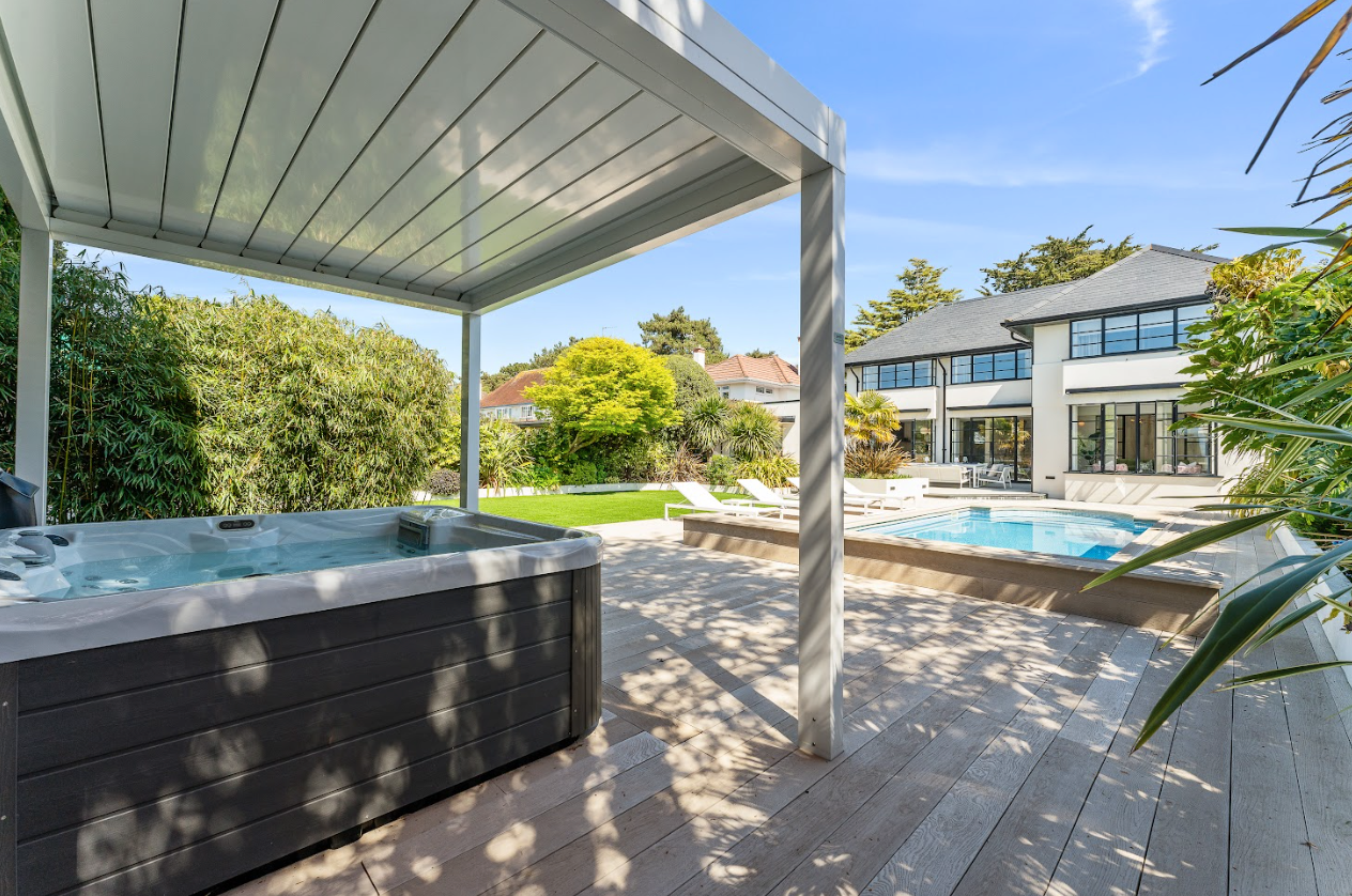 A hot tub is sitting under a pergola next to a swimming pool.