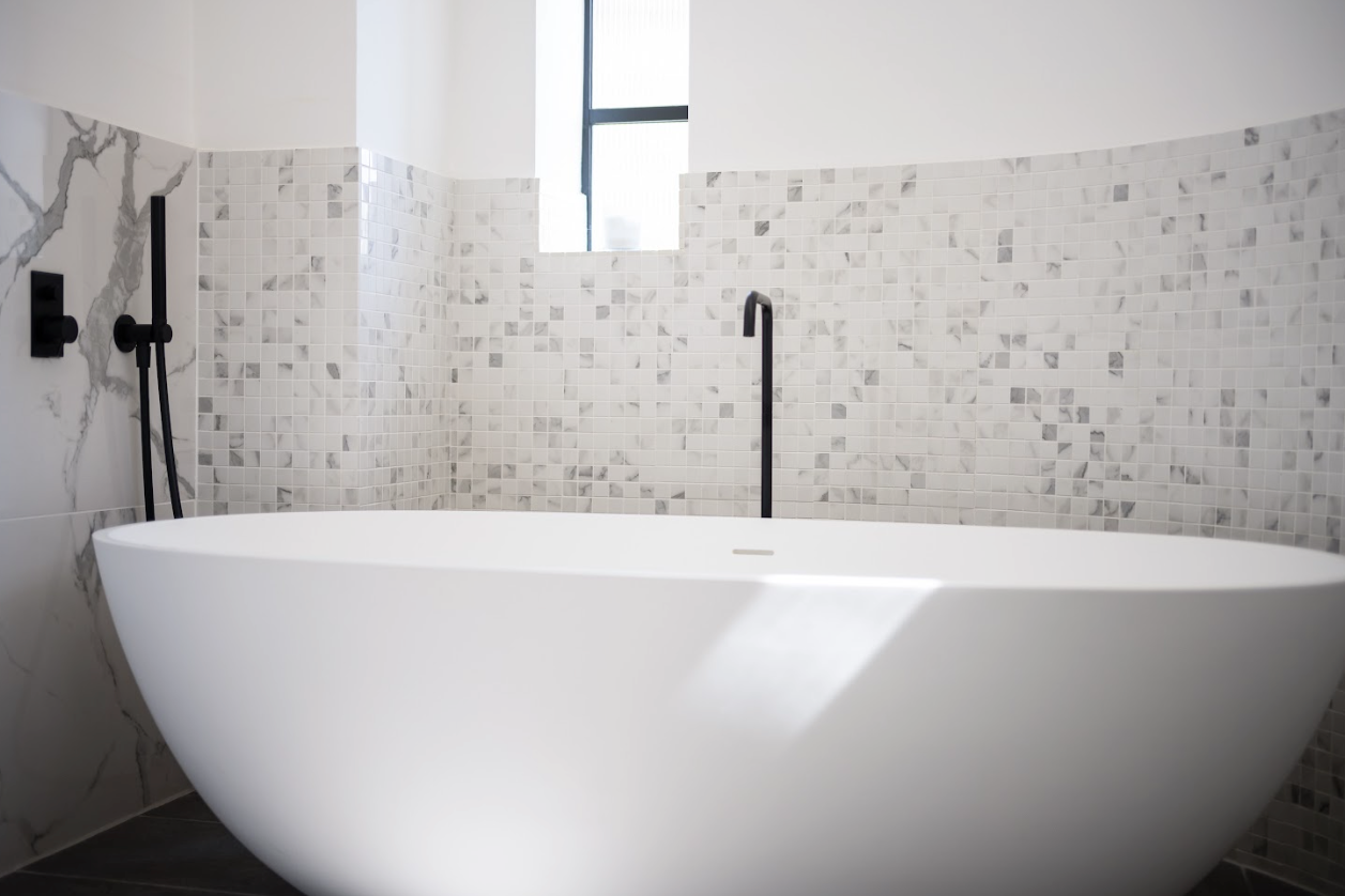 A large white bathtub is sitting in a bathroom next to a window.