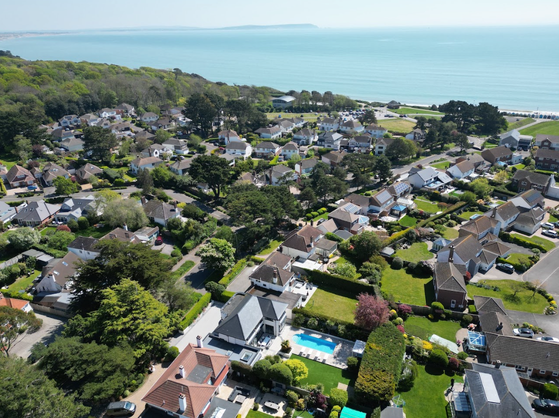 An aerial view of a residential area with a pool and the ocean in the background.