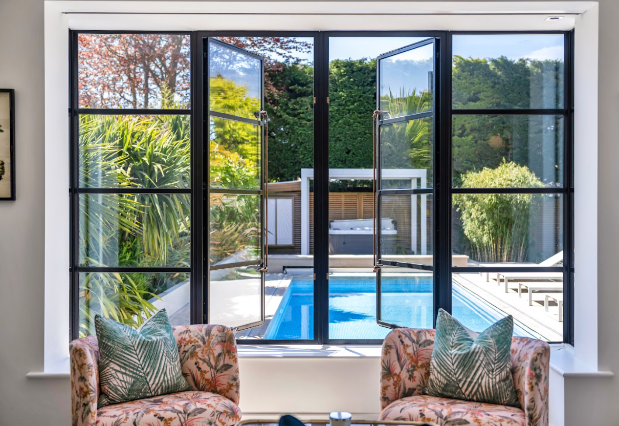 A living room with a couch and chairs and a view of a pool through a window.