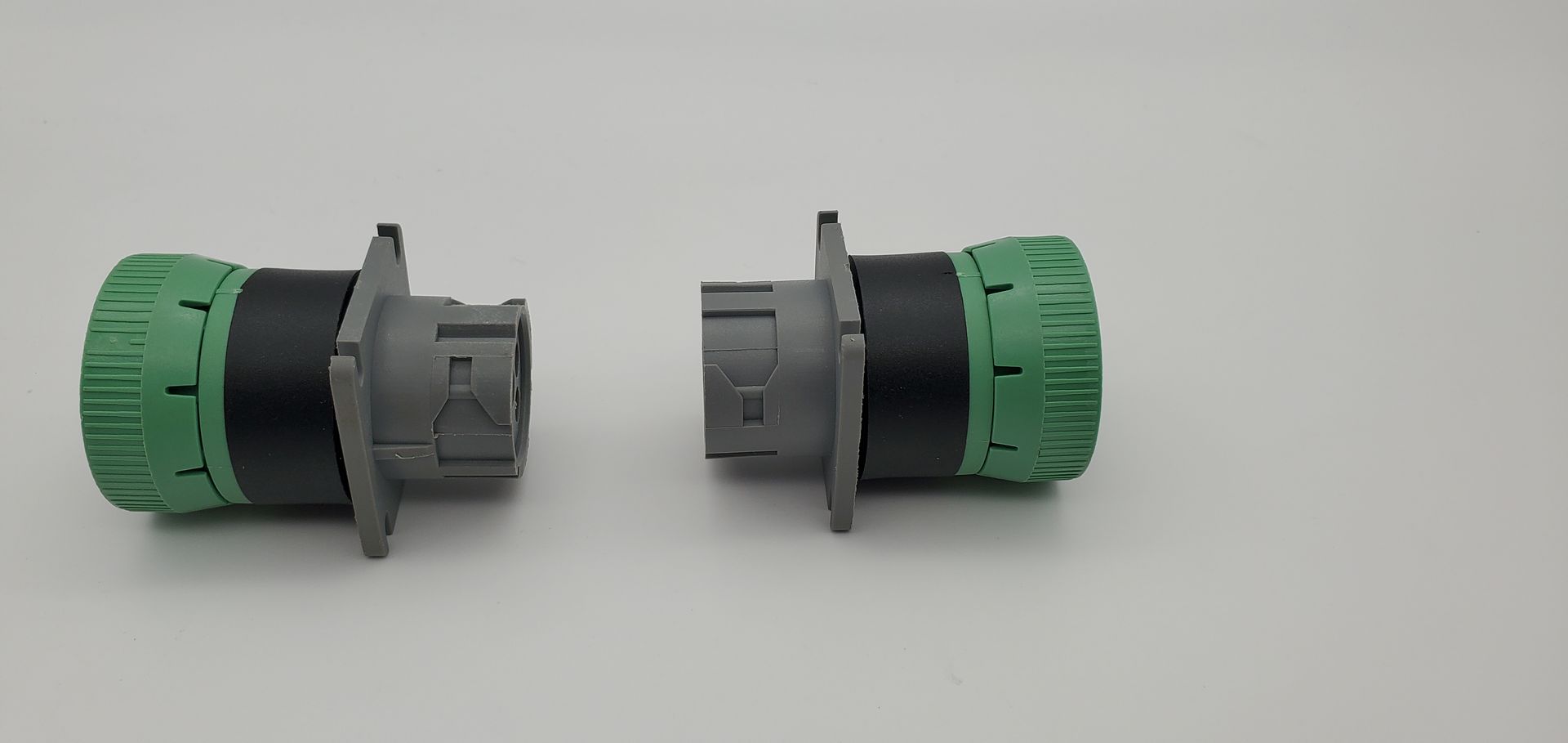 Two green and gray connectors are sitting next to each other on a white surface.