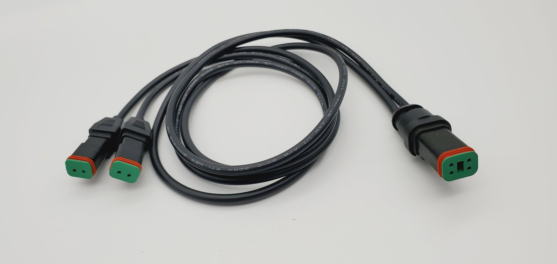 A black cable with two green connectors on a white surface.