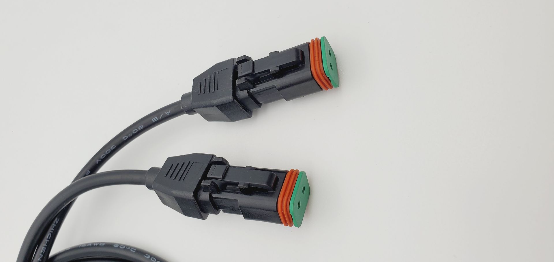 Two black cables with green connectors are connected to each other on a white surface.