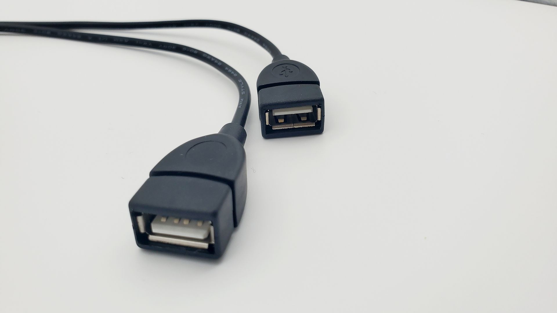 Two black usb cables are connected to each other on a white surface.