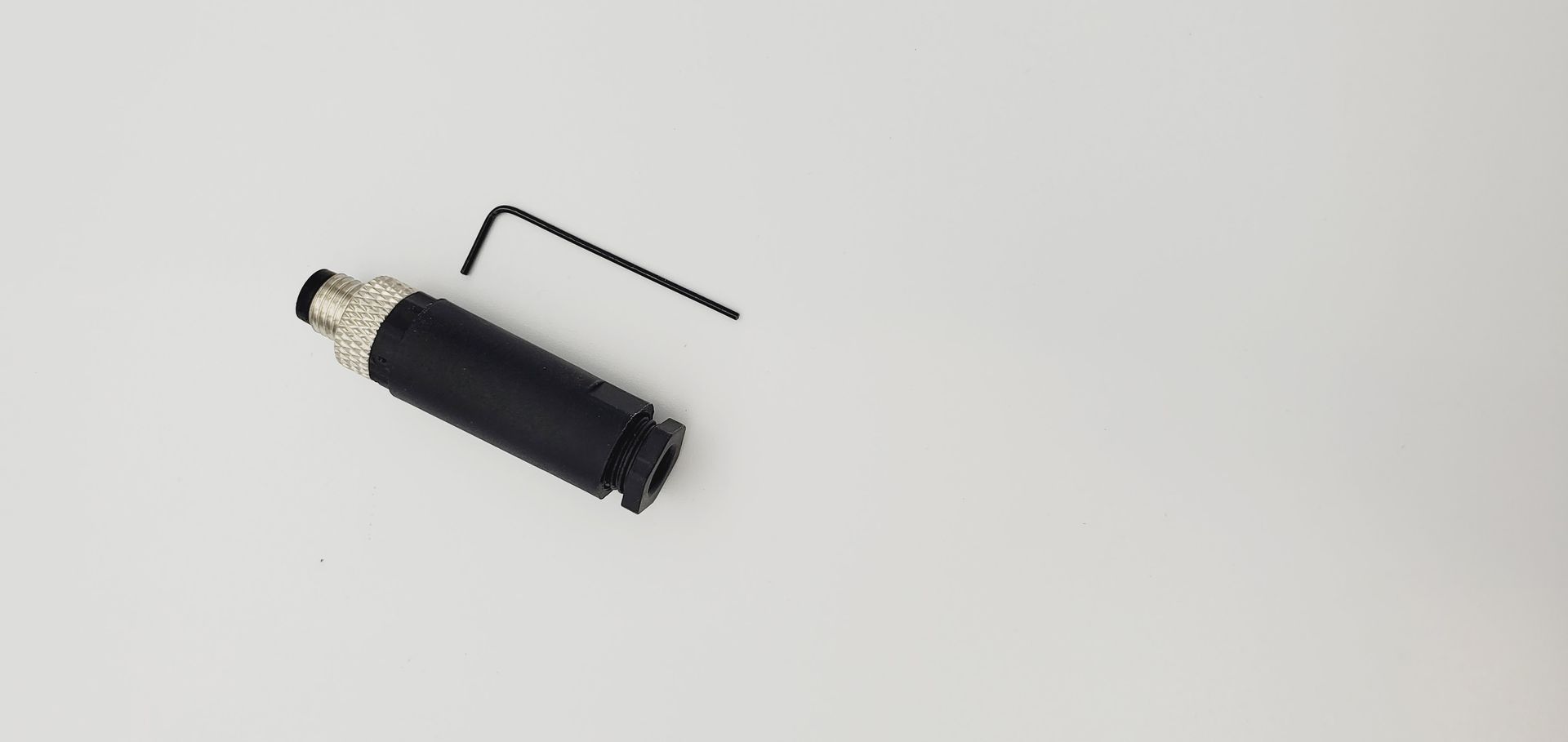 A small black object with a wrench attached to it is sitting on a white surface.