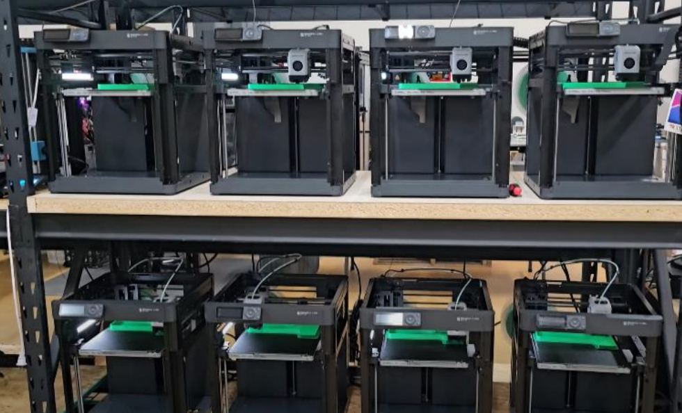 A row of 3d printers sitting on top of a wooden table.