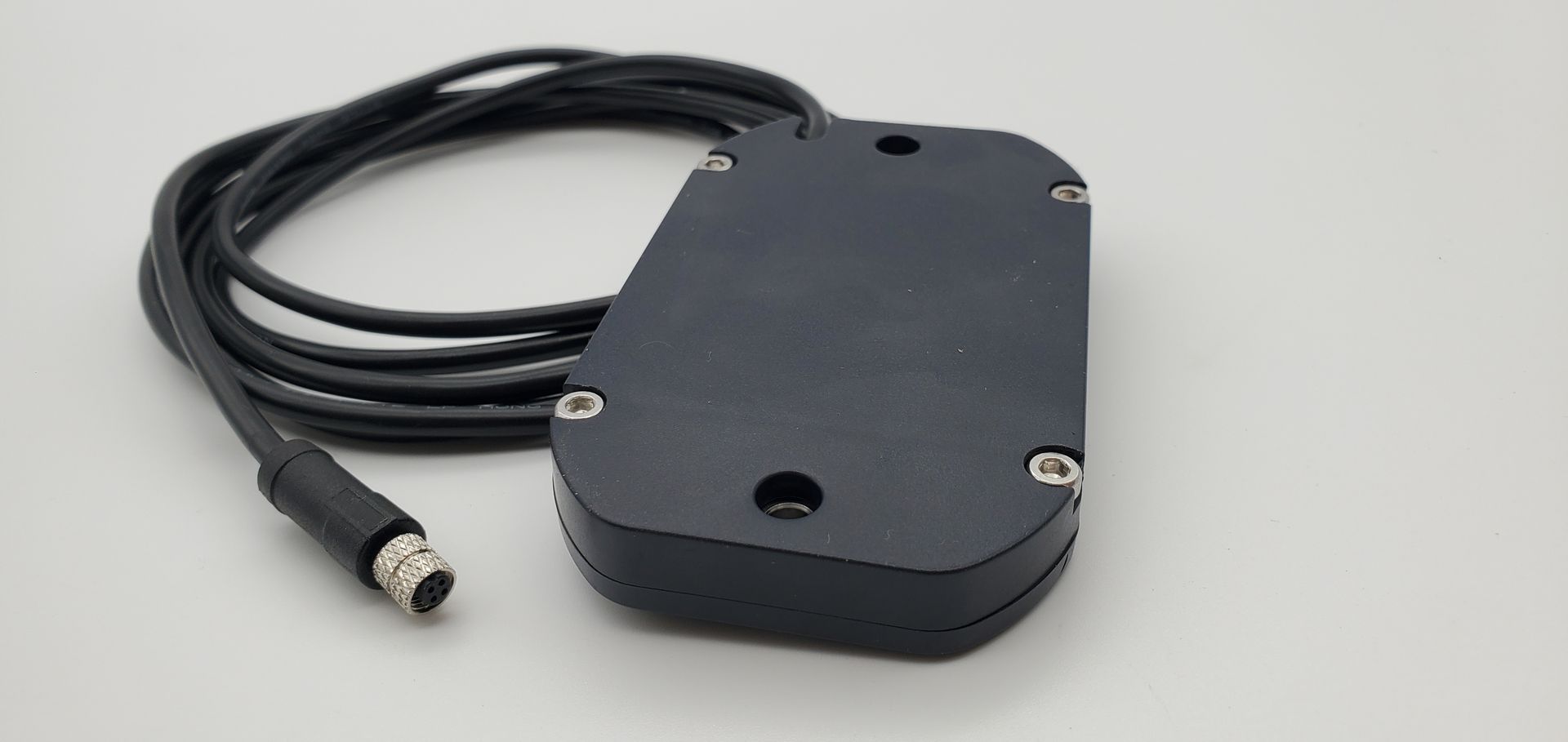 A black device with a cable attached to it is sitting on a white surface.