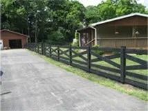 A wooden fence along a dirt road in front of a house.