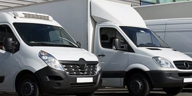 Two white vans are parked next to each other in a parking lot.