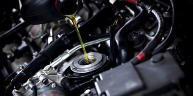 A close up of a person pouring oil into a car engine.