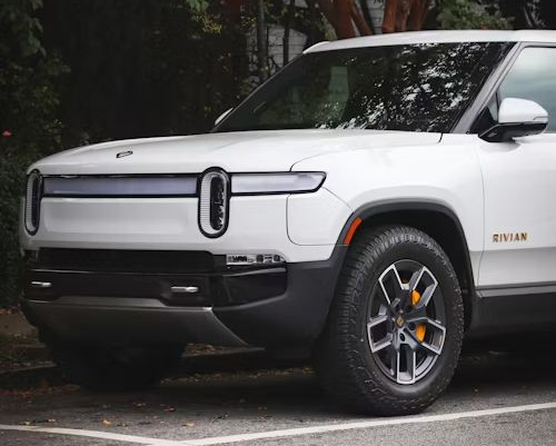 White Rivian electric SUV, front view, parked on a street. Black and gray accents, orange brake calipers.
