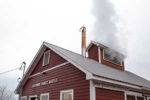 Red maple syrup building with smoke billowing from the chimney.