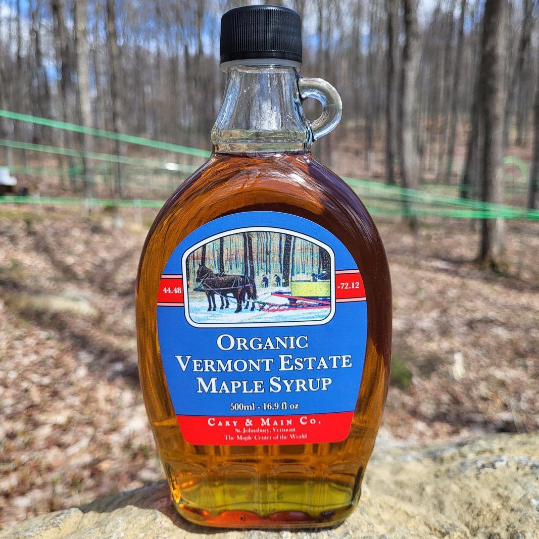 Bottle of organic Vermont maple syrup with a blue and red label; set outdoors.