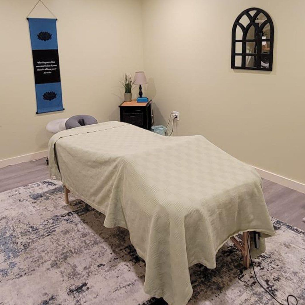 Massage room with a table covered in a light green blanket, a rug, and wall decor.