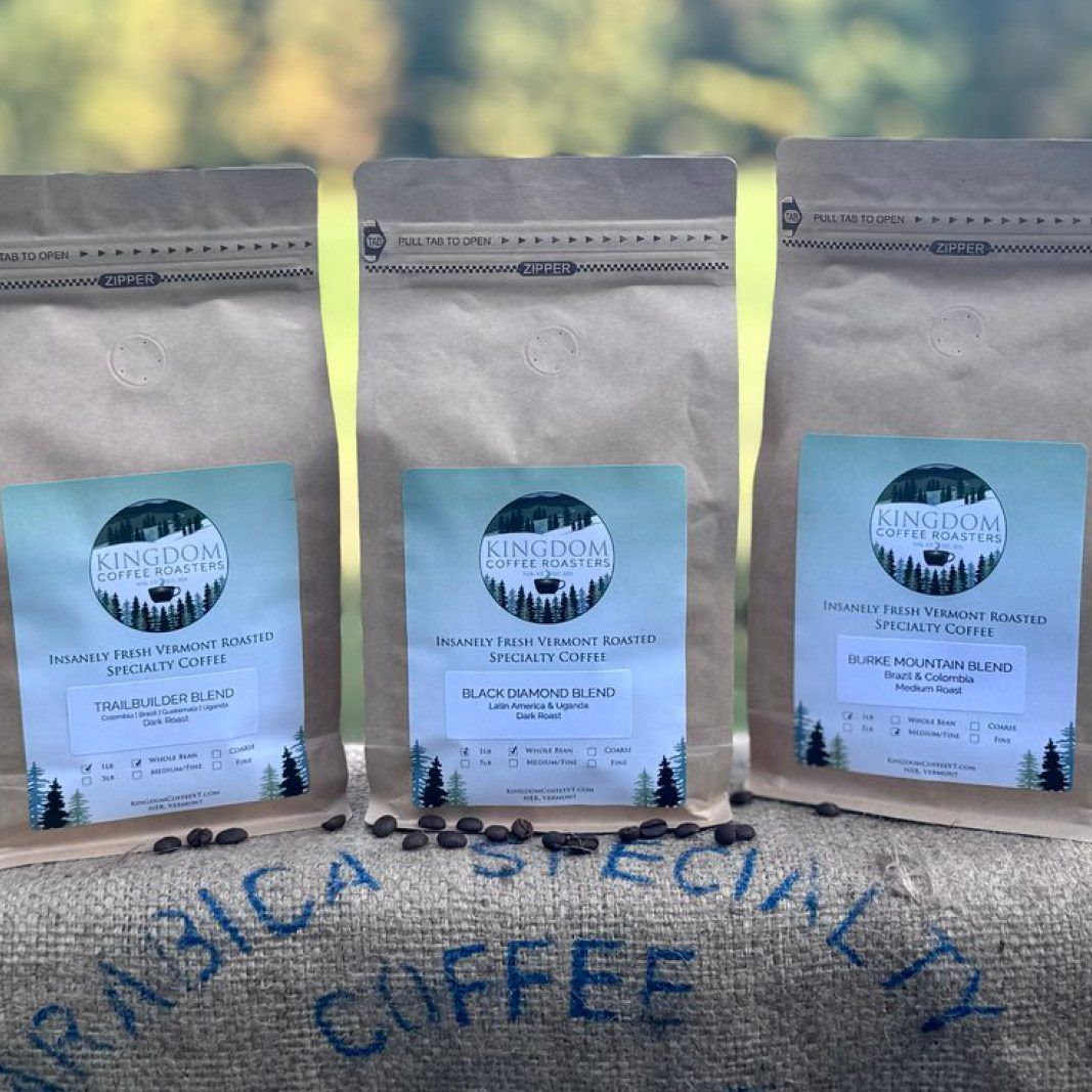 Three bags of specialty coffee sit on a burlap sack. Each bag has a label with a logo and coffee type.