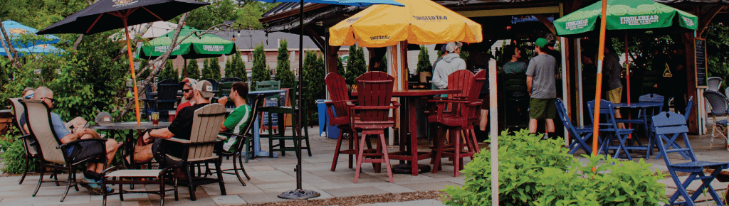 Outdoor patio with tables, chairs, umbrellas and people seated. Red, yellow, and green umbrellas.
