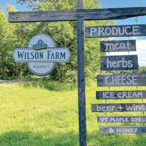 Sign for Wilson Farm Market with product listings: produce, meat, herbs, cheese, ice cream, beer, wine, maple syrup, honey.