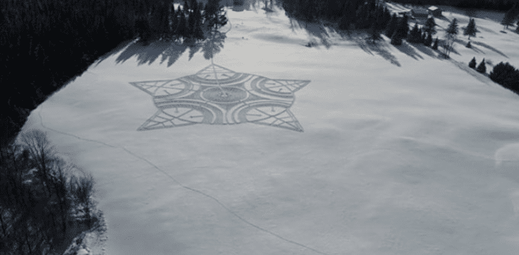 Aerial view of a star-shaped pattern carved into snow, surrounded by a forest and a snowy landscape.