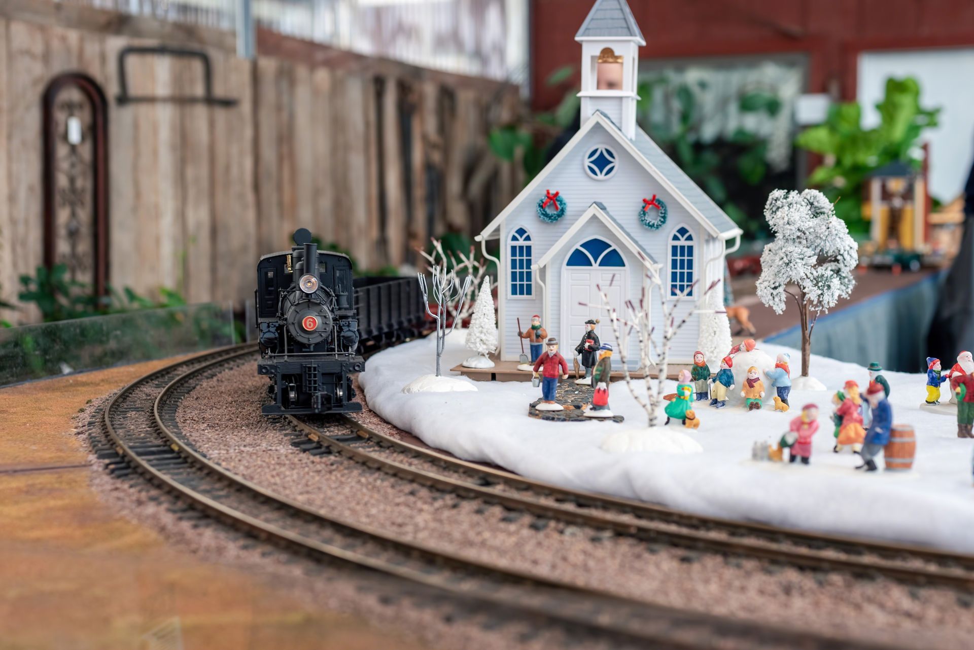 Model train passing a snowy church scene with miniature figures.