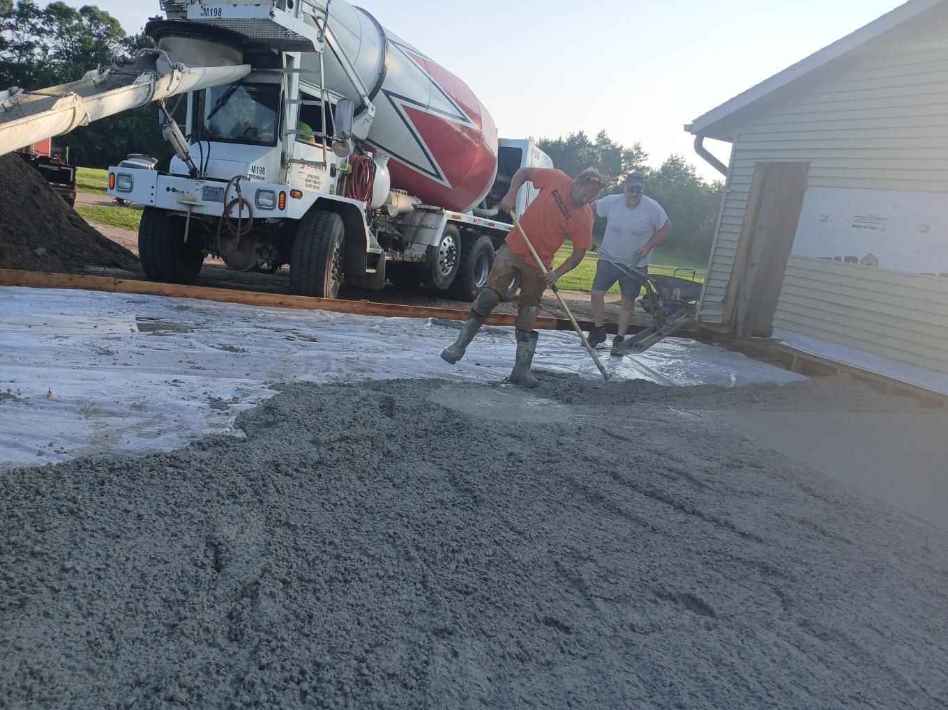 Concrete being poured on a driveway by a truck, men spreading it with rakes.
