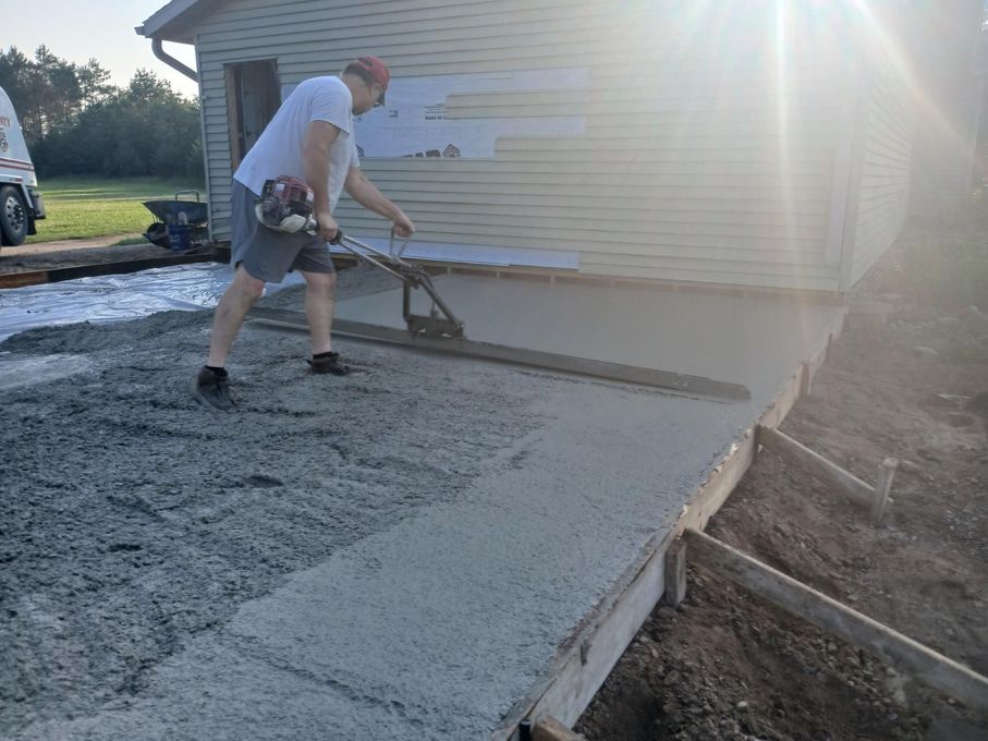 Man using power screed to level wet concrete for a walkway near a building.