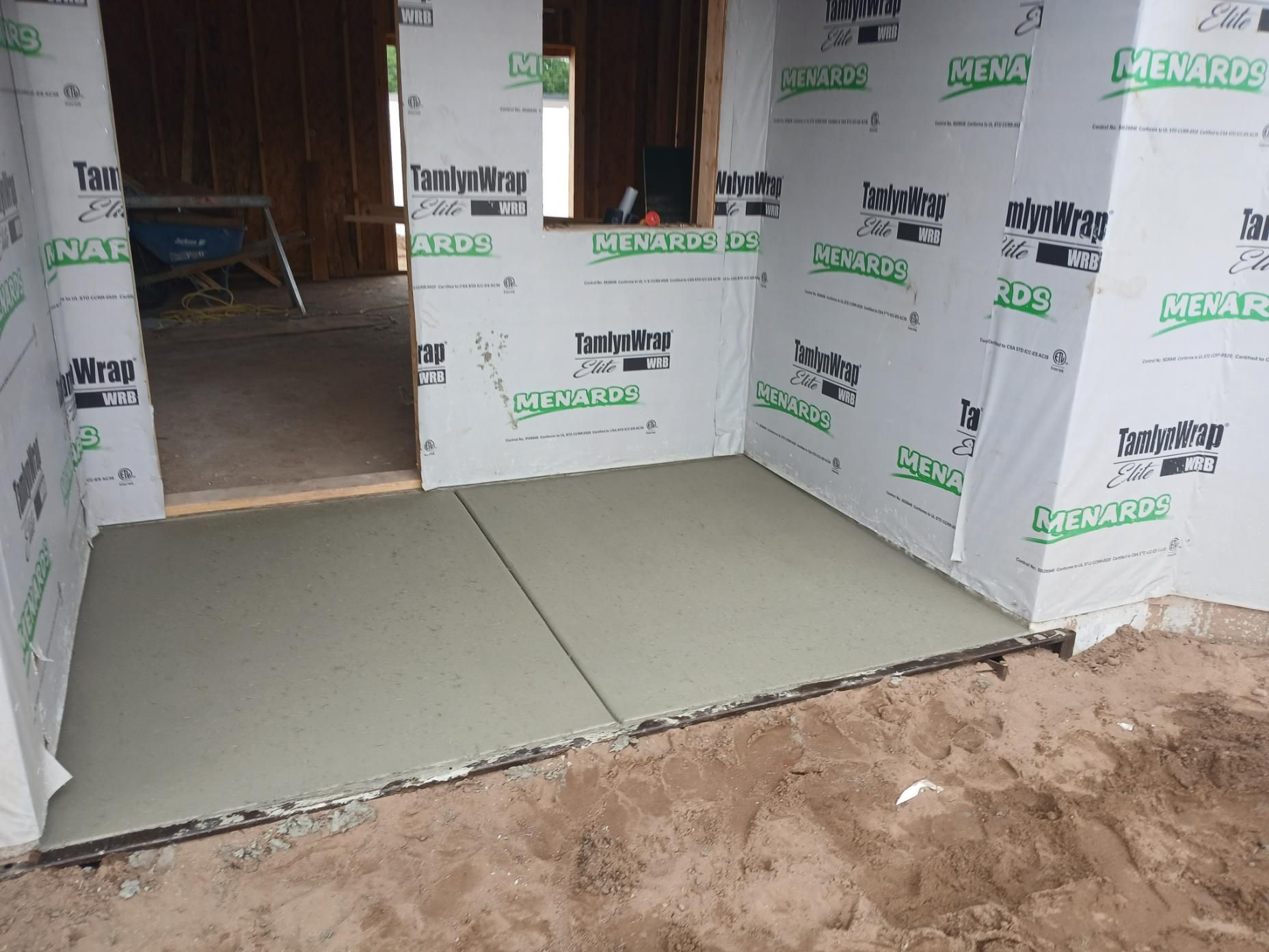 Concrete patio under construction, enclosed by a building's framing and covered with protective wrap.