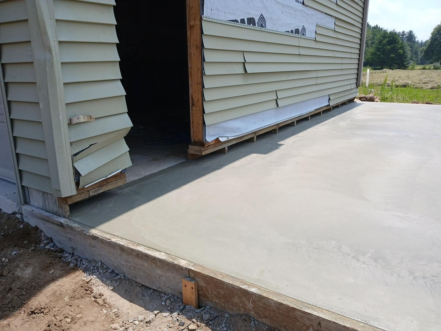 Exterior view of a newly poured concrete slab beside a building with damaged siding.