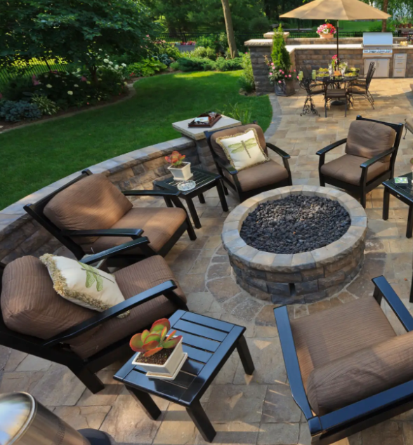 Patio with seating around a fire pit; grass and outdoor kitchen in the background.